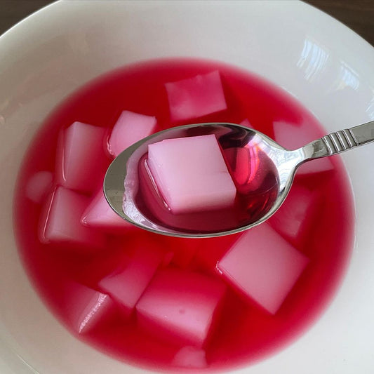 Pink rose mahalepi pudding cubes served in bright rose syrup in a white bowl, with one cube lifted on a spoon.