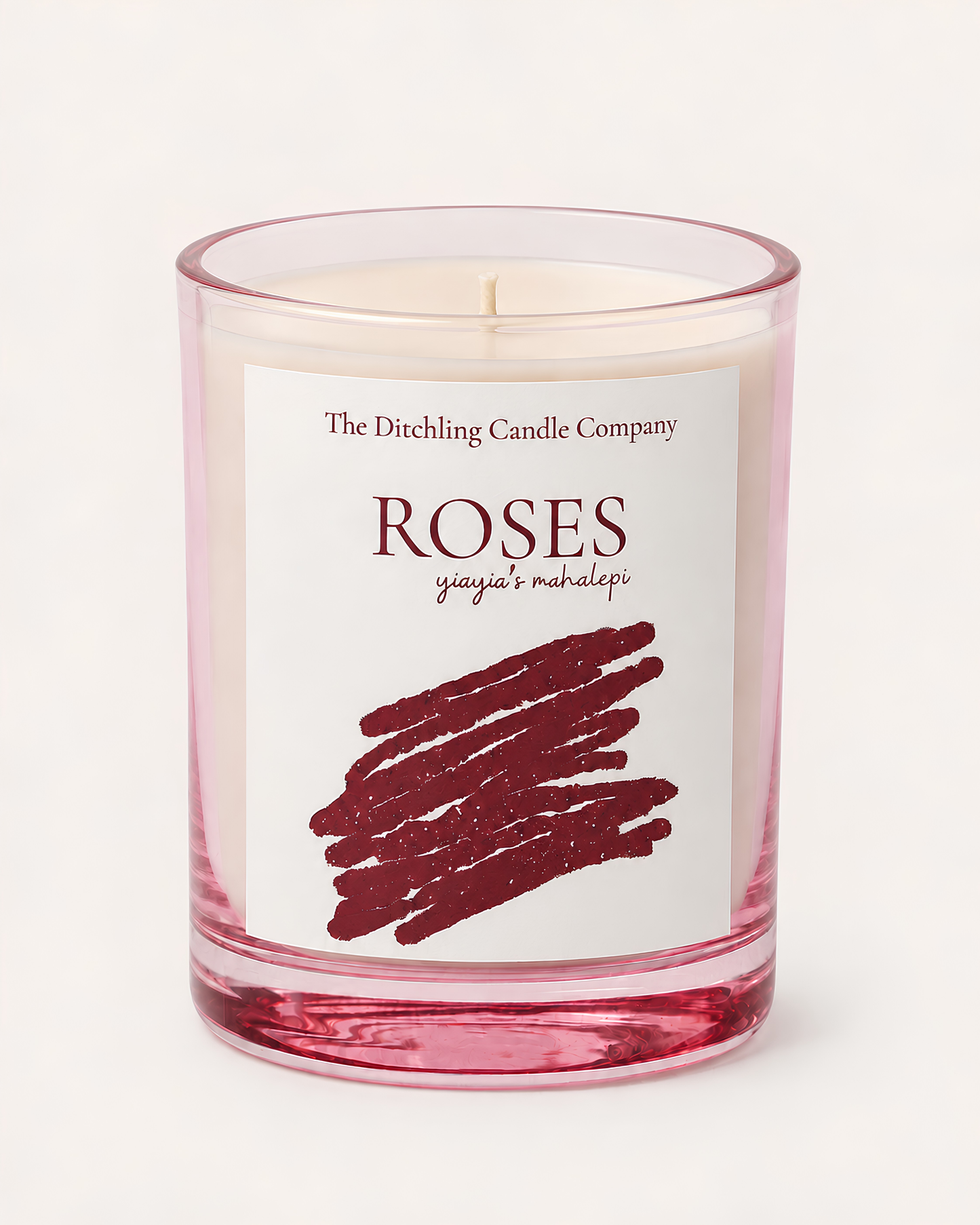 A glass jar soy scented candle with a white label reading 'The Ditchling Candle Company ROSES yiayia's mahalepi' featuring a burgundy scribble graphic on a light rose pink candle inside.